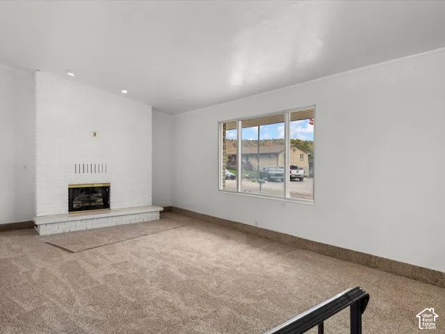 White painted brick fireplace with a raised hearth, large picture window, and neutral carpeting