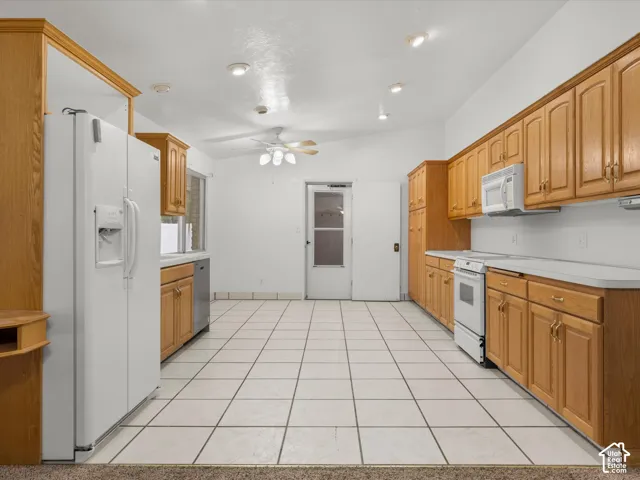 Kitchen featuring natural wood cabinetry, white appliances, solid surface countertops, tile flooring, and recessed lighting