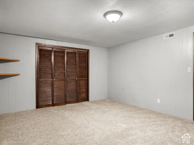 Room featuring wall-to-wall carpeting, wood-finish paneling, louvered closet doors, and built-in shelving