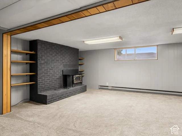 Interior room featuring a brick-surround fireplace with wood-burning stove insert, built-in wooden shelving, and neutral carpeting