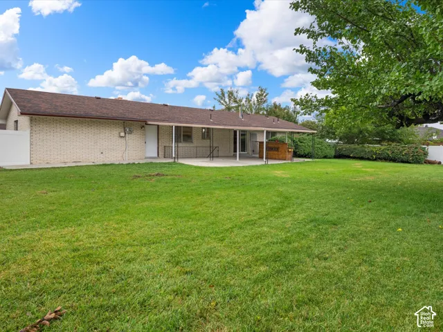 Brick exterior, expansive lawn, covered patio, and perimeter vinyl fencing
