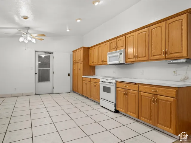 Kitchen featuring extensive wood cabinetry, white countertops, built-in range, mounted microwave, and ceramic tile flooring
