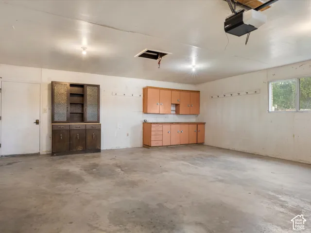 Attached garage featuring concrete flooring, integrated storage cabinetry, built-in shelving with glass-paneled doors, and a wall-mounted hook system