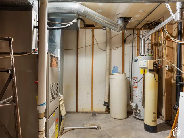 Mechanical room featuring a high-efficiency furnace, a dedicated water heater, and a water softening system with exposed wall studs and concrete flooring