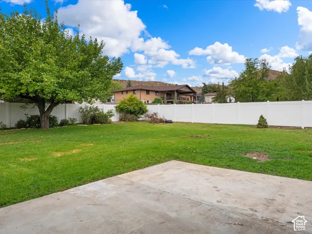 Expansive backyard featuring a concrete patio, a full-height white vinyl privacy fence, mature trees, and a manicured lawn