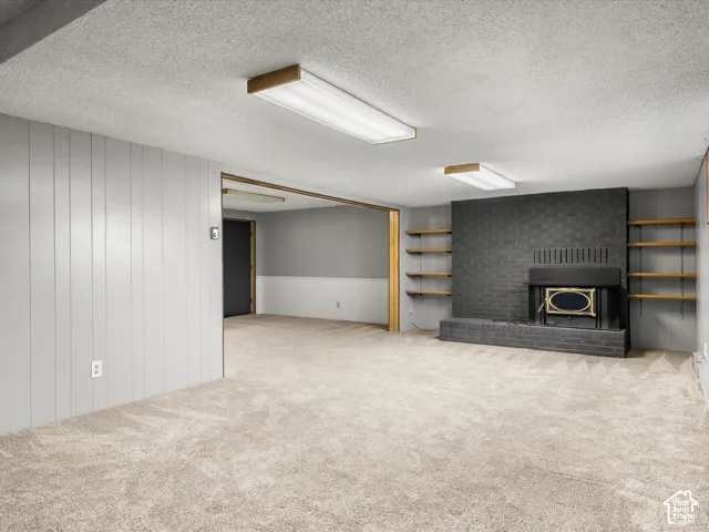 Interior space featuring a painted brick fireplace, built-in wooden shelving, neutral carpeting, and panel wall detailing