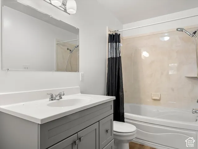 Bathroom featuring a grey vanity with a white integrated sink, polished chrome faucet, full-width mirror with attached light fixture, and a tub-shower combination with a surround