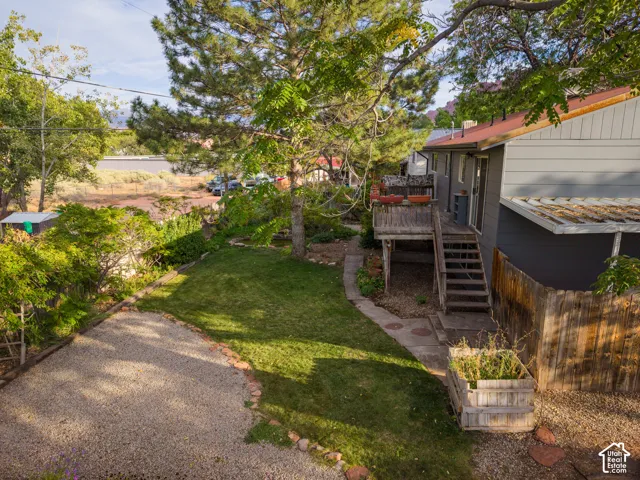 Gravel drive, mature trees, manicured lawn, wooden deck, and raised garden beds
