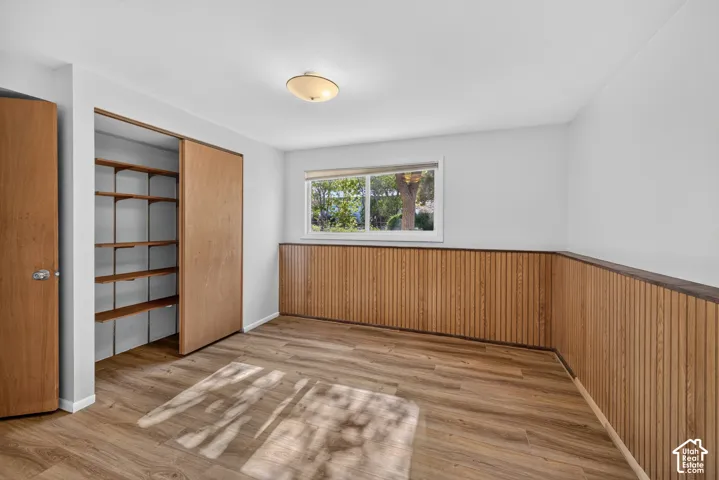 Wood-finish flooring, built-in closet shelving, wood paneling, and a flush mount ceiling light fixture