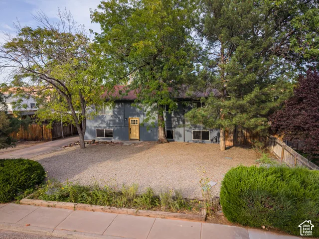 Split-level exterior featuring a gravel front yard, mature trees, and a wooden entry door