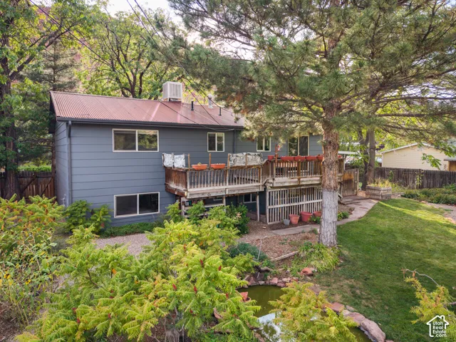 Multi-level wood deck, corrugated metal roof, mature tree, manicured lawn, and a koi pond