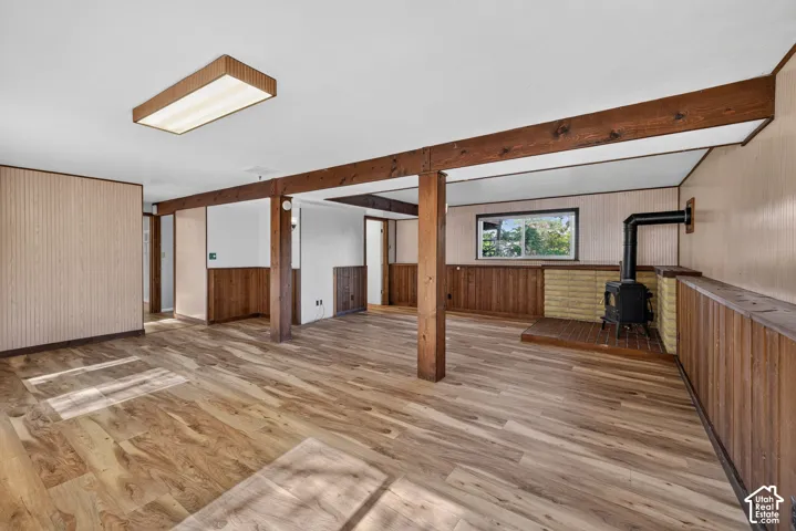 Wood-finish flooring, exposed wood beams, and a black wood-burning stove with a brick hearth