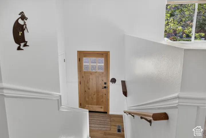 Natural wood door with privacy glass panels, wood-finish flooring, and white painted walls
