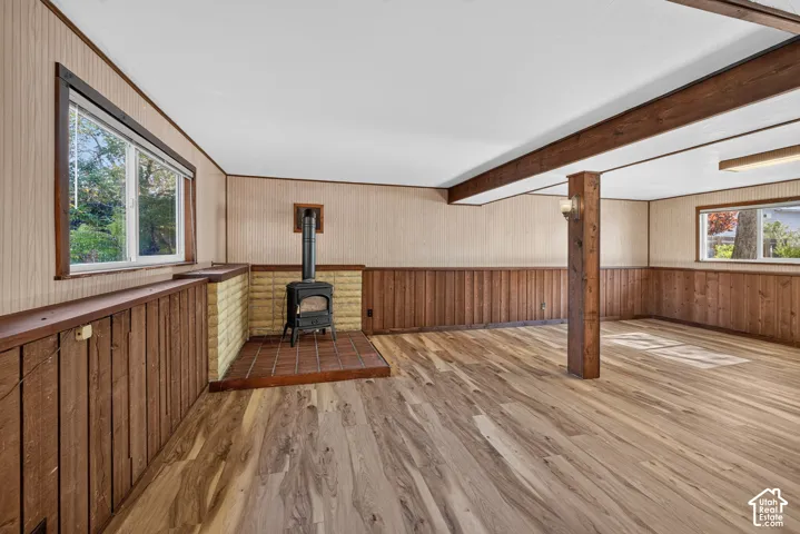 Wood-finish flooring, exposed wood beams, wood paneling, a wood-burning stove with a brick and tile hearth, and multiple windows