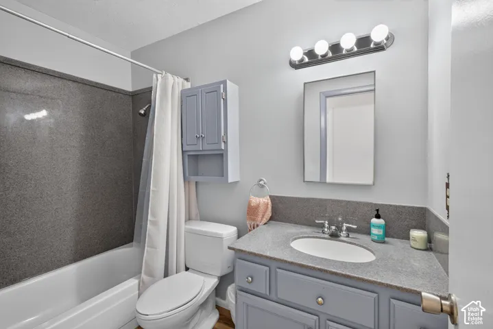 White bathtub with a gray-patterned shower surround, a white toilet, and wood-finish flooring