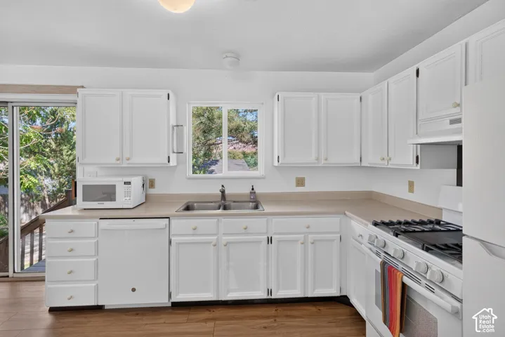 White cabinetry, wood-finish flooring, dual basin sink, gas range, and sliding glass door