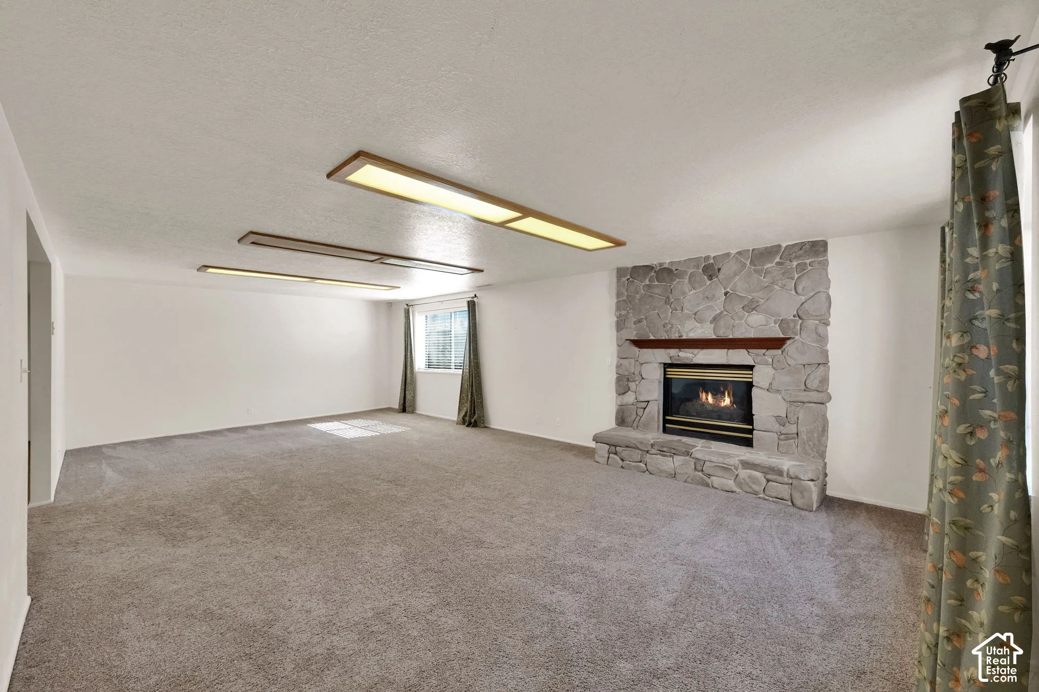 Expansive room featuring a stone-clad gas fireplace with a wood mantel, soft gray carpeting, and integrated ceiling lighting