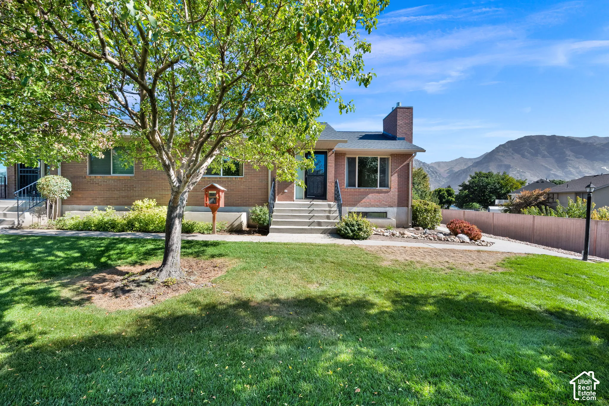 Brick exterior with a prominent chimney, established front yard landscaping, and substantial mature trees