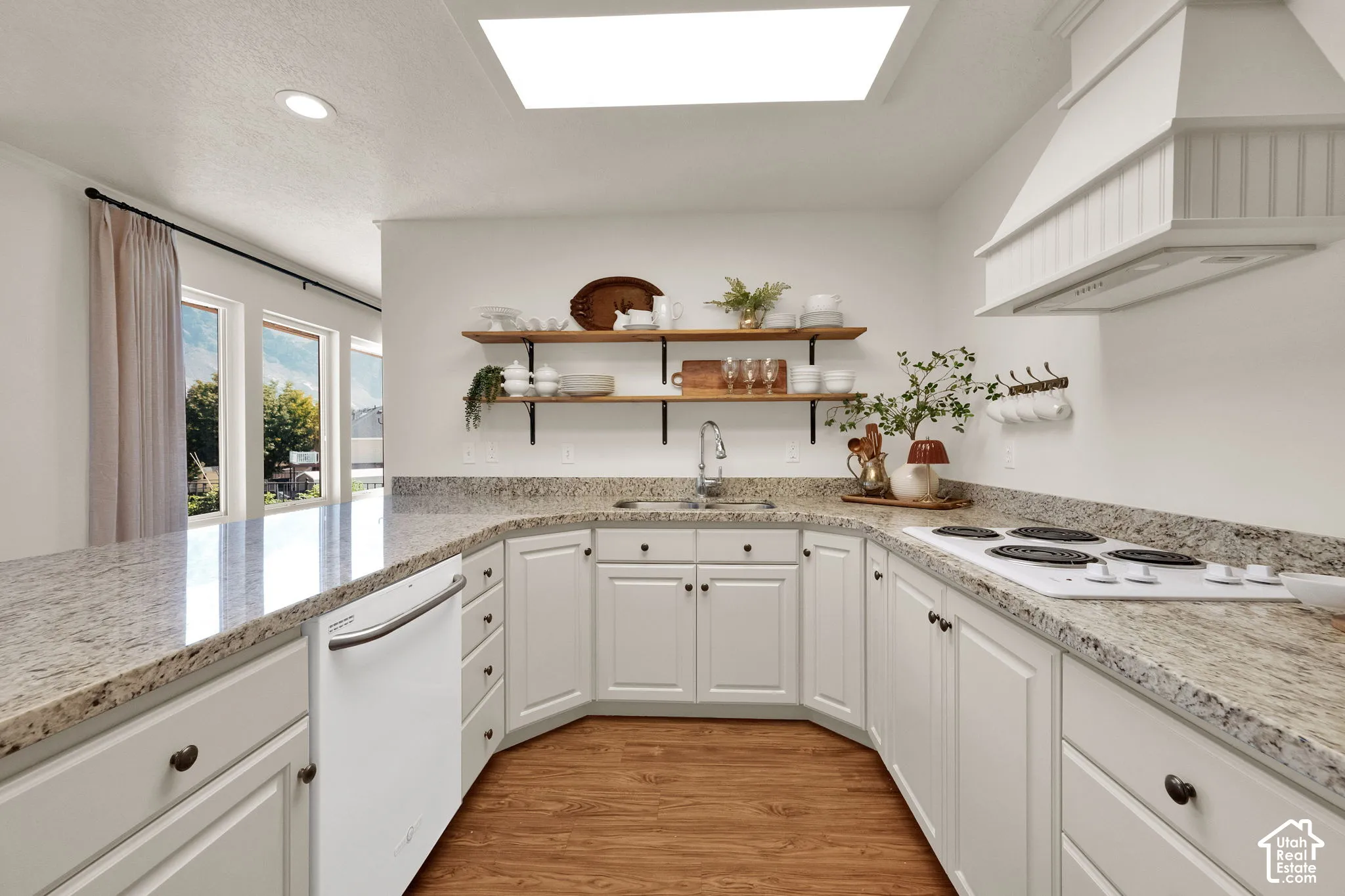 U-shaped kitchen with light toned cabinetry, granite countertops, wood-finish flooring, a white range, and a white dishwasher