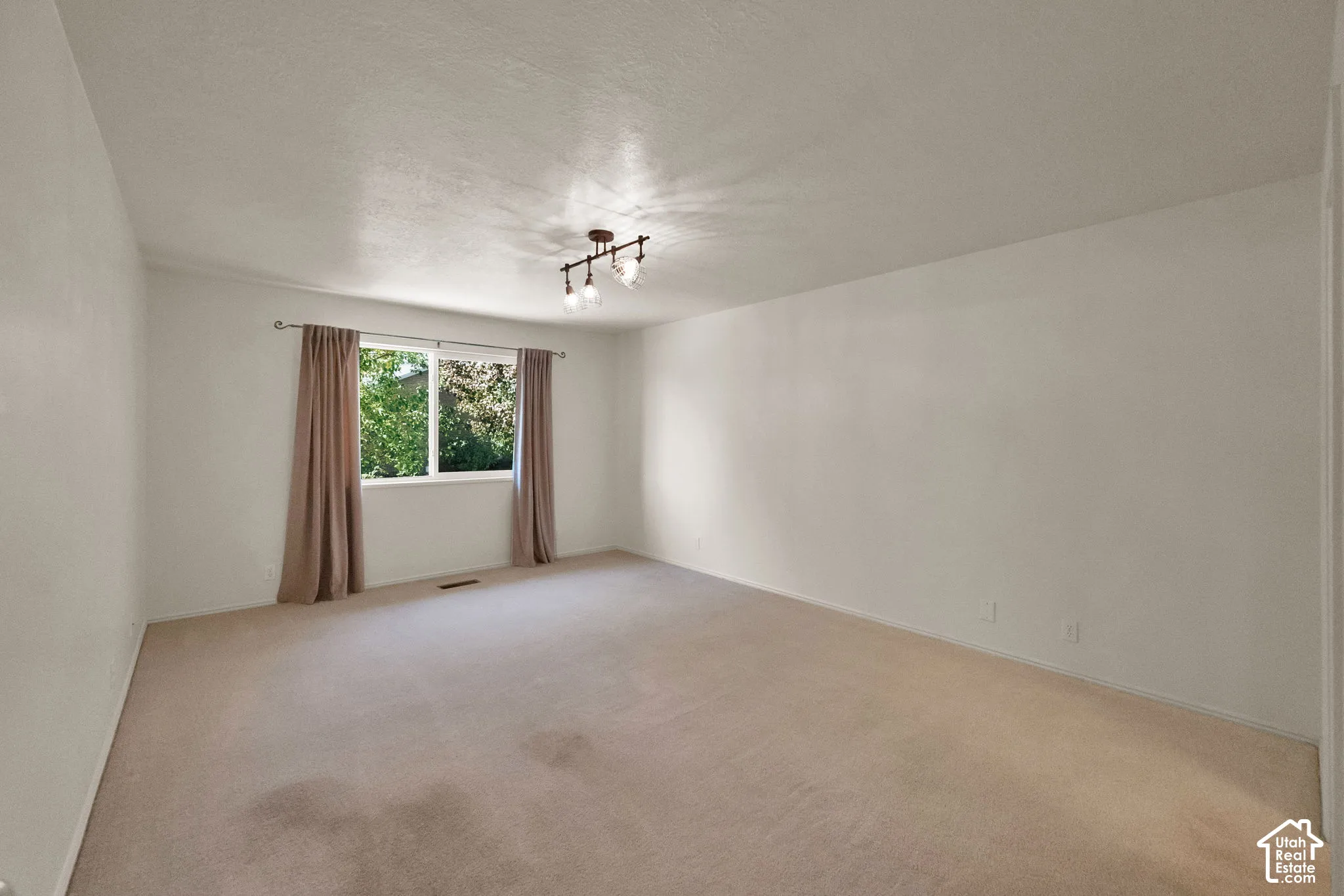 Spacious room, light-colored carpet, and a large window with natural light