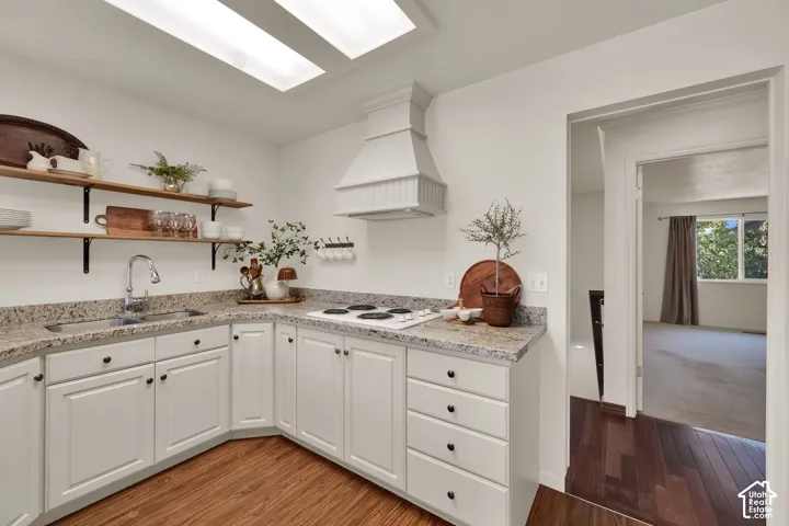 Kitchen featuring light toned cabinetry, wood-finish flooring, granite countertops, open shelving, and a built-in range hood