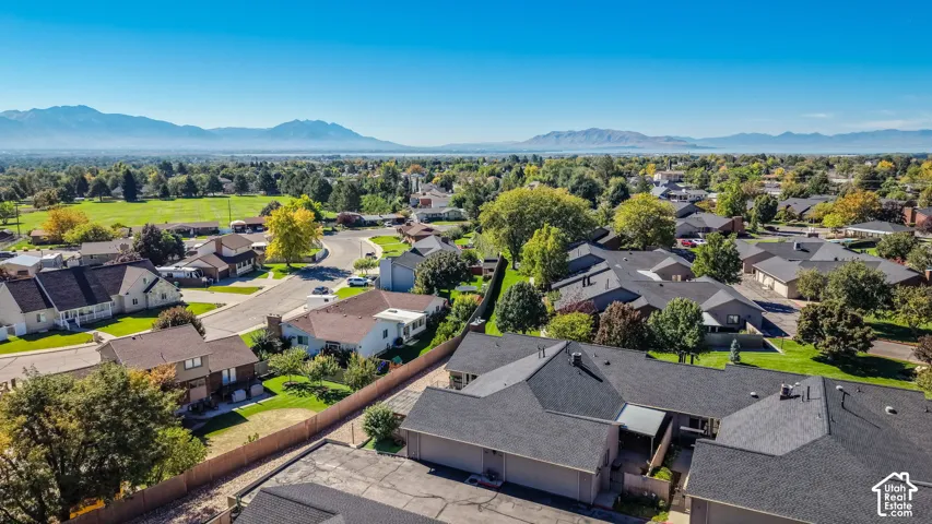 Aerial overview of the neighborhood, featuring residential properties with asphalt shingle roofs and mature trees, surrounded by distant mountains