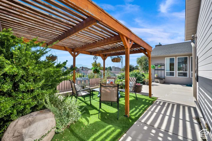 Wood pergola structure over a patio with artificial turf, bordered by mature shrubs and a concrete pathway