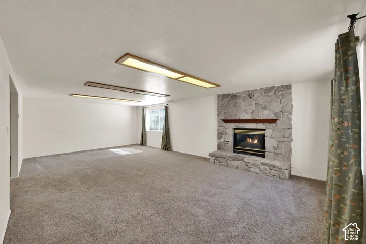Expansive room featuring a stone-clad gas fireplace with a wood mantel, soft gray carpeting, and integrated ceiling lighting
