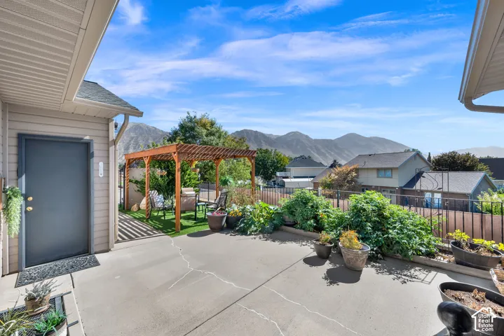 Concrete patio with a wood pergola, raised garden beds, and a fenced perimeter