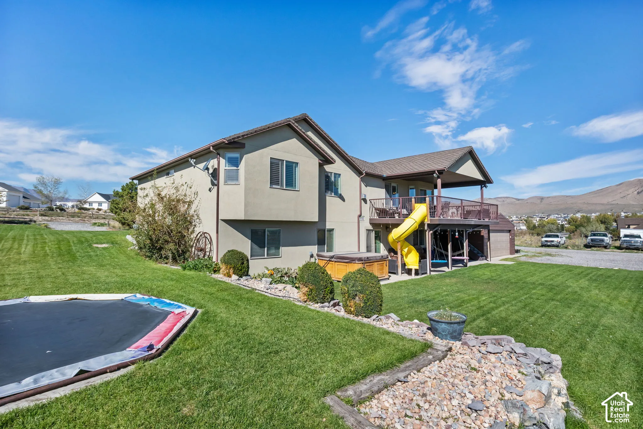 Expansive backyard with manicured lawn, established landscaping, and a multi-level deck featuring an exterior spa