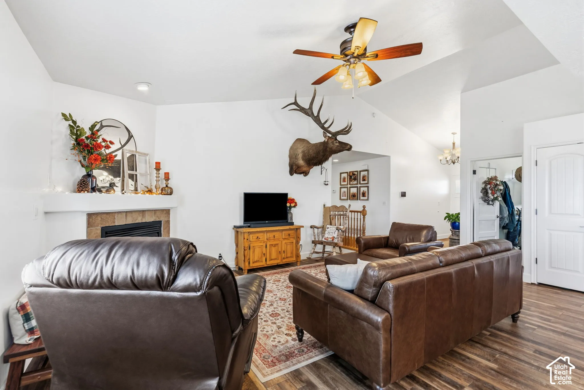 Vaulted ceiling with an attached ceiling fan, corner fireplace with tile surround, wood-finish flooring, and white interior doors