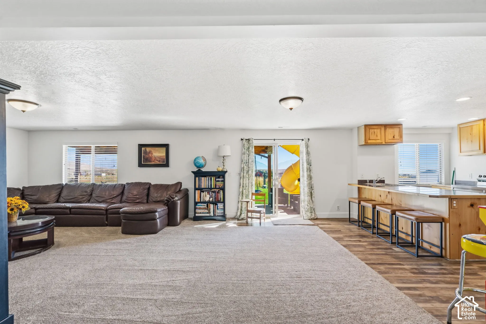 Open-concept living space featuring a carpeted area, wood-finish flooring, a kitchen island with seating, a sliding glass door, and recessed lighting