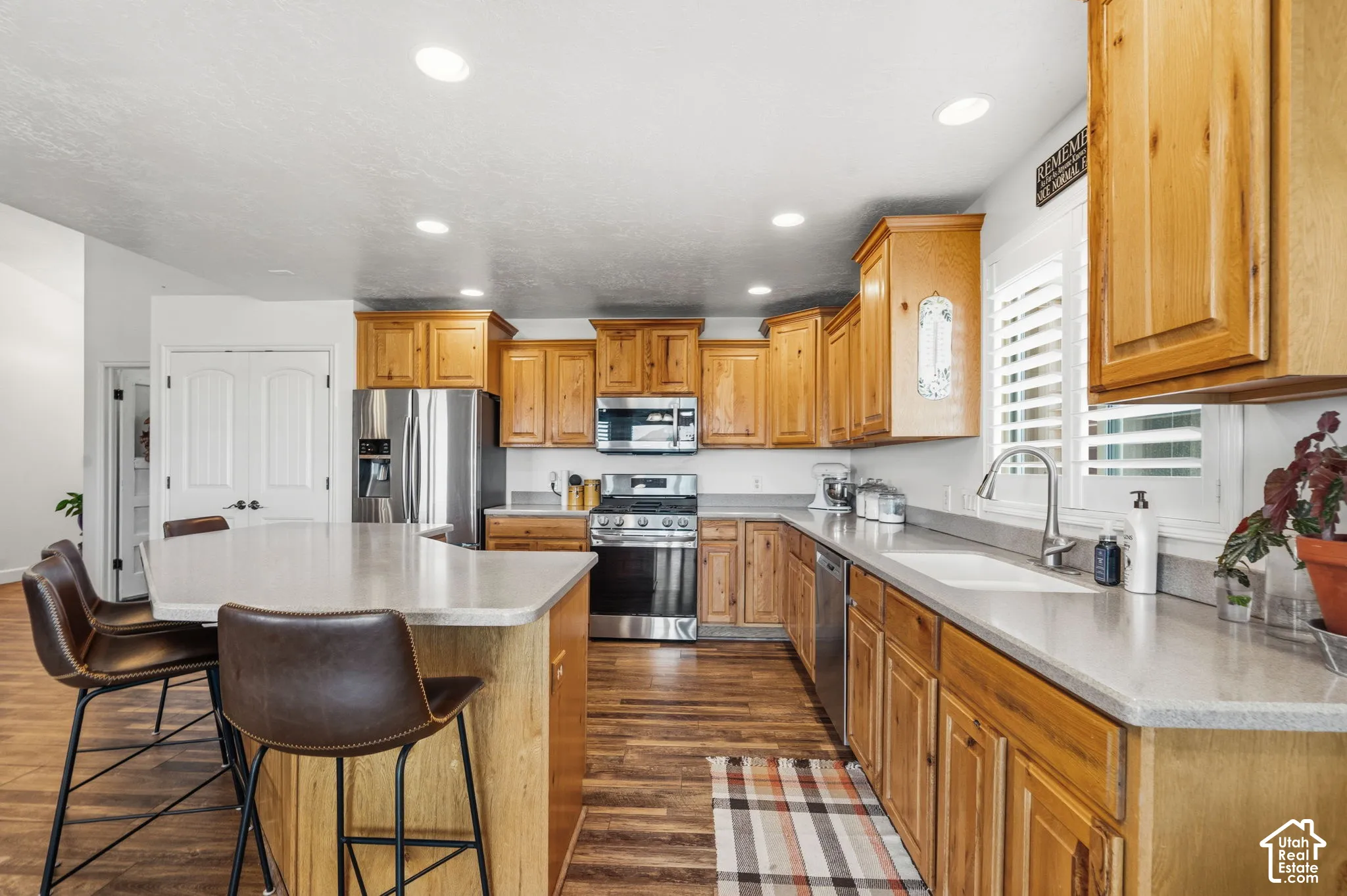 Open-concept kitchen featuring wood-finish flooring, light wood cabinetry, stone countertops, and stainless steel appliances