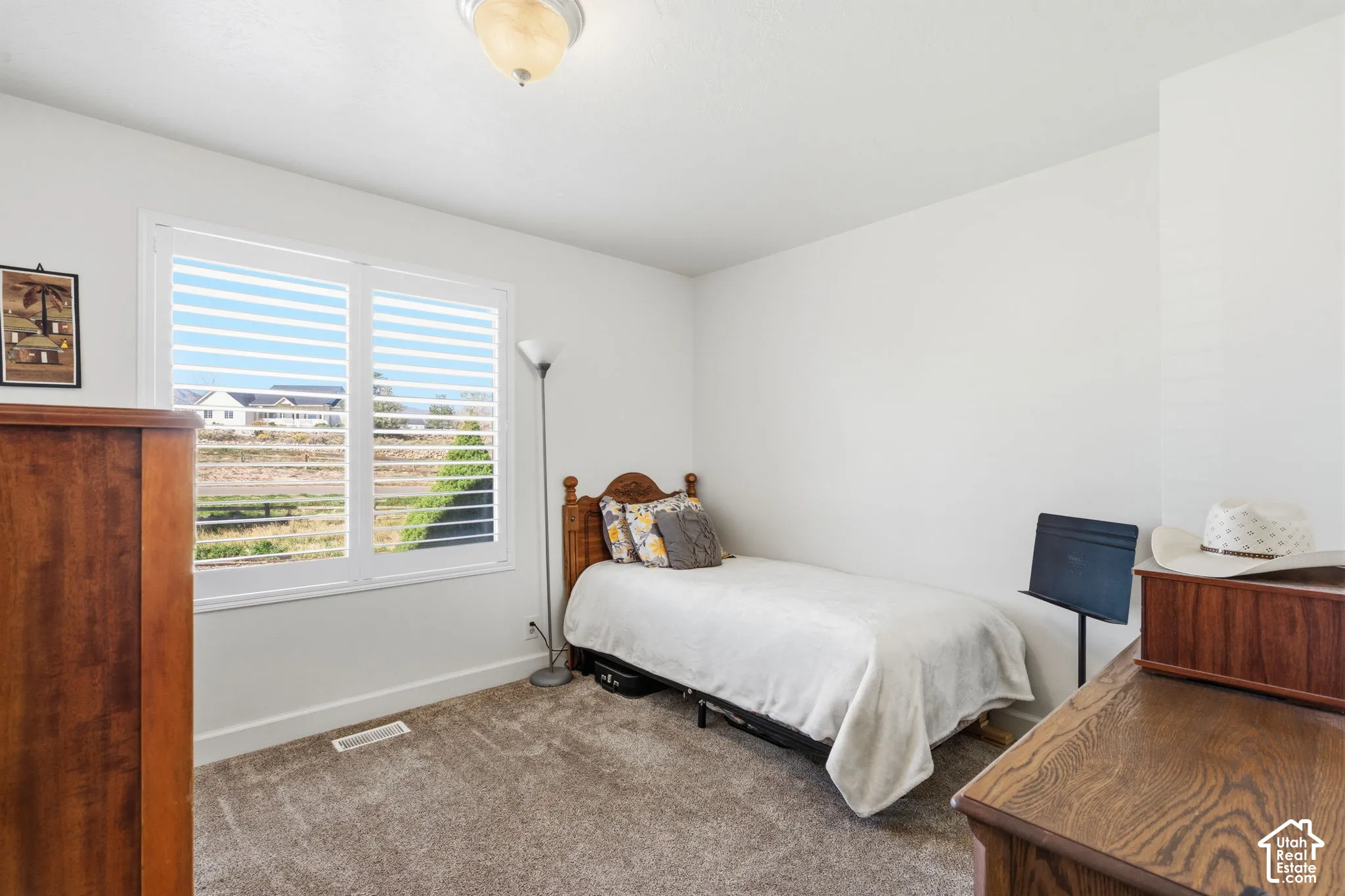 Neutral wall color with plush carpet flooring, showcasing a window with plantation shutters