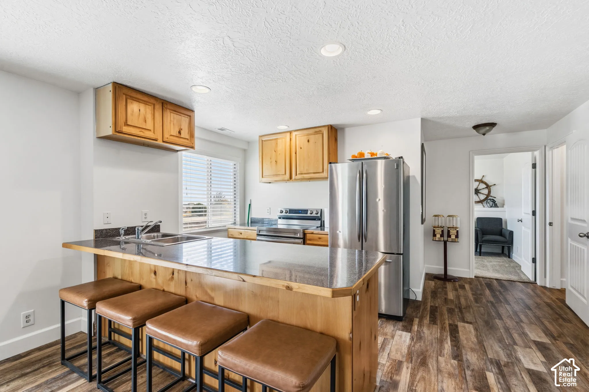 Wood-finish flooring throughout, stainless steel appliances, wood cabinetry, built-in breakfast bar, and recessed lighting