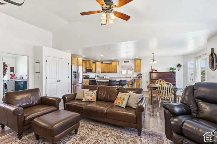 Vaulted ceilings with a ceiling fan, wood-finish flooring, kitchen with stainless steel appliances and wood cabinetry, and a dining area with pendant lighting