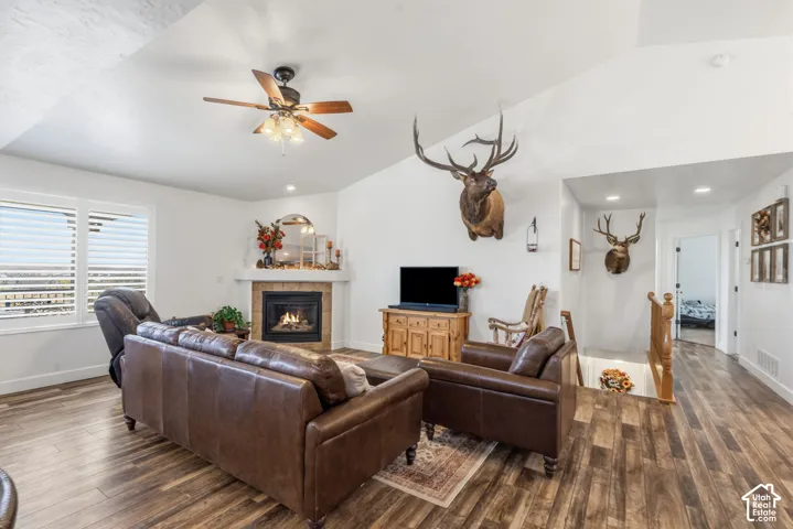 Vaulted ceiling with a ceiling fan, fireplace with a stone surround, wood-finish flooring, and white window shutters