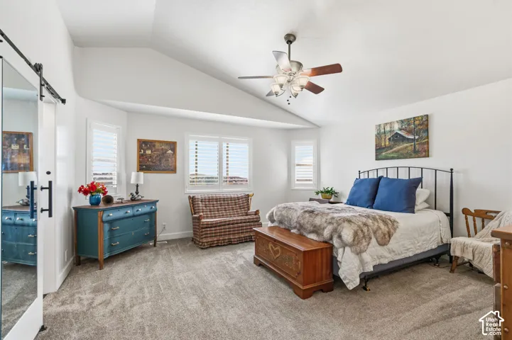 Vaulted ceiling with a ceiling fan, multiple windows with plantation shutters, and light-colored carpeting