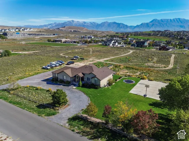 Expansive property featuring a gravel circular driveway, a manicured lawn, a concrete sports court, and distant mountain scenery