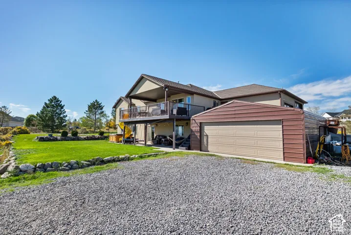 Expansive gravel driveway, covered upper-level deck, lower-level patio, and a separate metal-sided garage structure