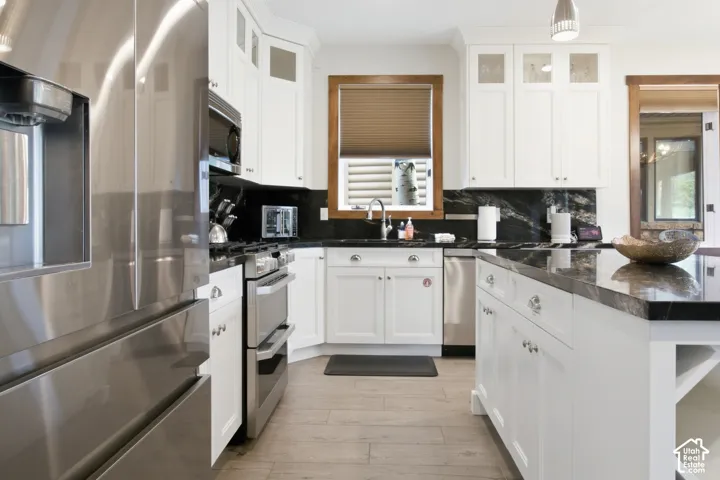 White cabinetry, dark stone countertops, stainless steel appliances, wood-finish flooring, and a central island