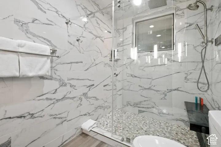 Glass-enclosed shower with full-height marble-look tile, pebble shower floor, built-in window, and a wall-mounted shower system