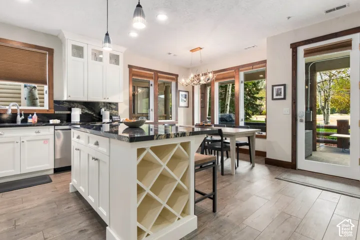 White cabinetry with glass-front accents, dark stone countertops, wood-finish flooring, and a central island with integrated wine storage