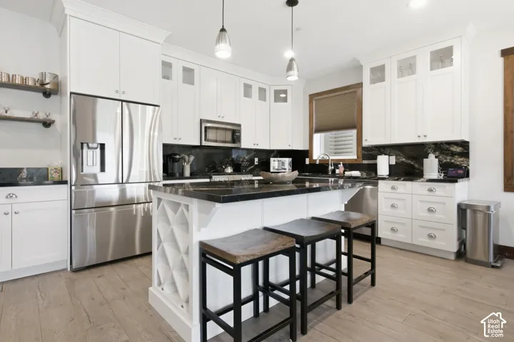 Kitchen with white cabinetry, stainless steel appliances, dark stone countertops, and wood-finish flooring