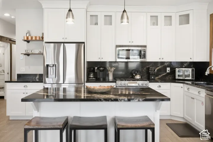 Gourmet kitchen with white cabinetry, black stone countertops and backsplash, stainless steel appliances, and a central island with pendant lighting