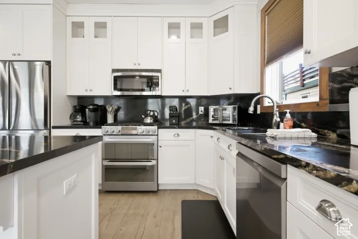 Kitchen featuring white cabinetry, dark stone countertops, stainless steel appliances, wood-finish flooring, and a stainless steel sink with a gooseneck faucet