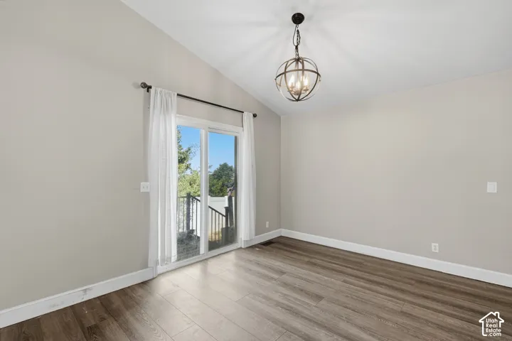 Wood-finish flooring, vaulted ceiling, and sliding glass door leading to an exterior balcony