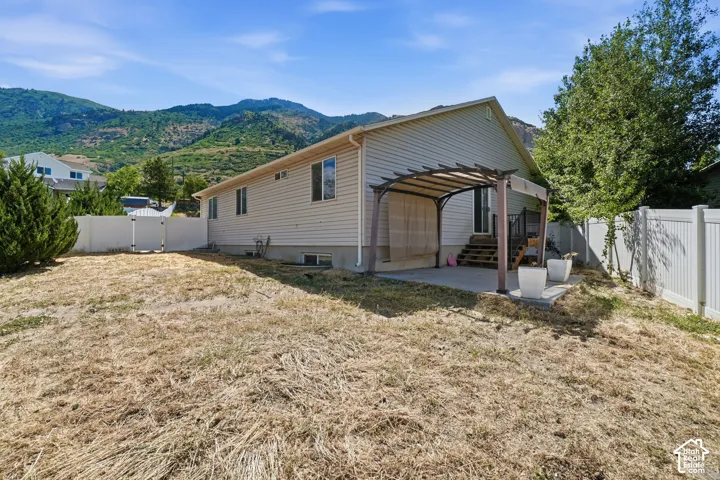 Rear exterior with a concrete patio, attached wood pergola, and white privacy fencing
