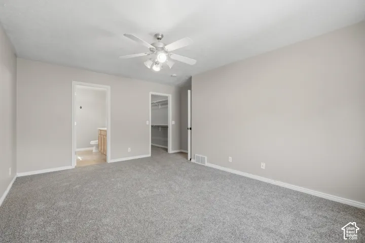 Spacious room featuring neutral carpeting, light-toned walls, and a ceiling fan