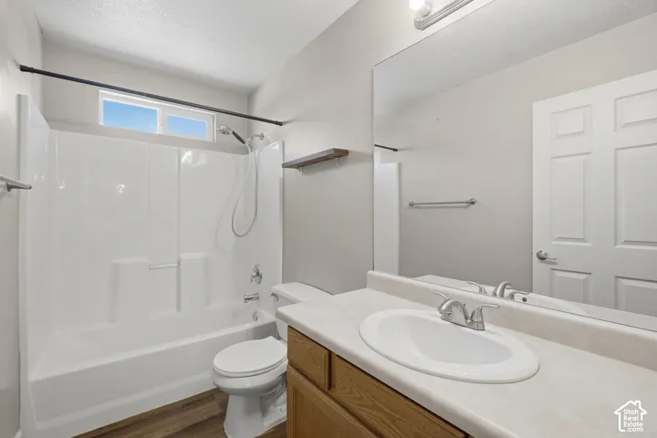 Tub/shower combination with a transom window, wood-finish flooring, single vanity with a laminate countertop, and a large wall-mounted mirror